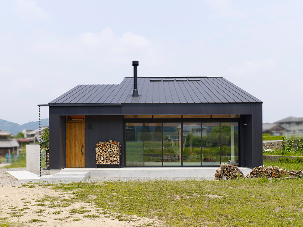 緑あふれる中に建つ黒しガルバリウム鋼板を貴重としたなかに、木のドアがアクセントとなったおしゃれな外観